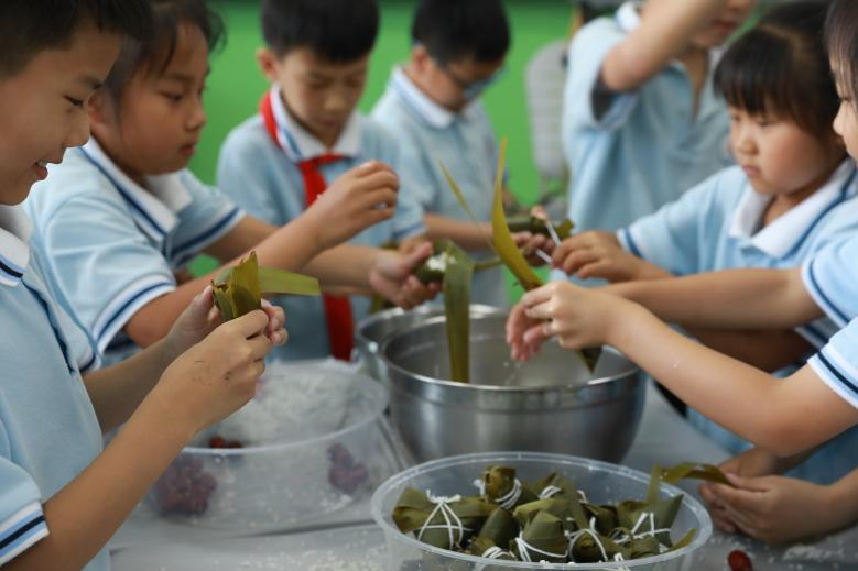 廊坊市第三十小学的端午节活动中,同学们在老师的带领下一起学习包粽子。
