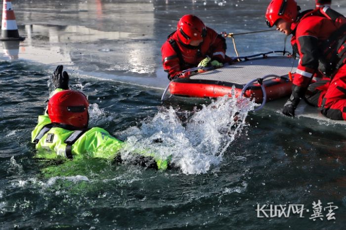 救援人员身着专业装备，在冰面上开展冰面救援演练，一名队员正破冰入水模拟遇险场景，其他队员在冰面借助救援设备随时准备实施营救。